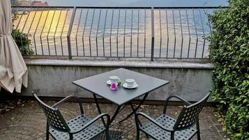 Une terrasse avec une table dressée pour deux personnes, offrant une vue sur un plan d’eau et des montagnes.