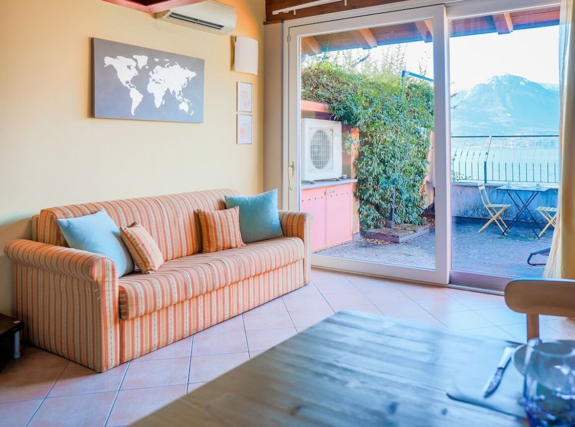 A room with a striped sofa, a table, and a sliding glass door leading to a balcony with a view of mountains.