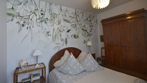 Et soveværelse med seng, et natbord, en lampe, en træskab og en væg med blomstret tapet.