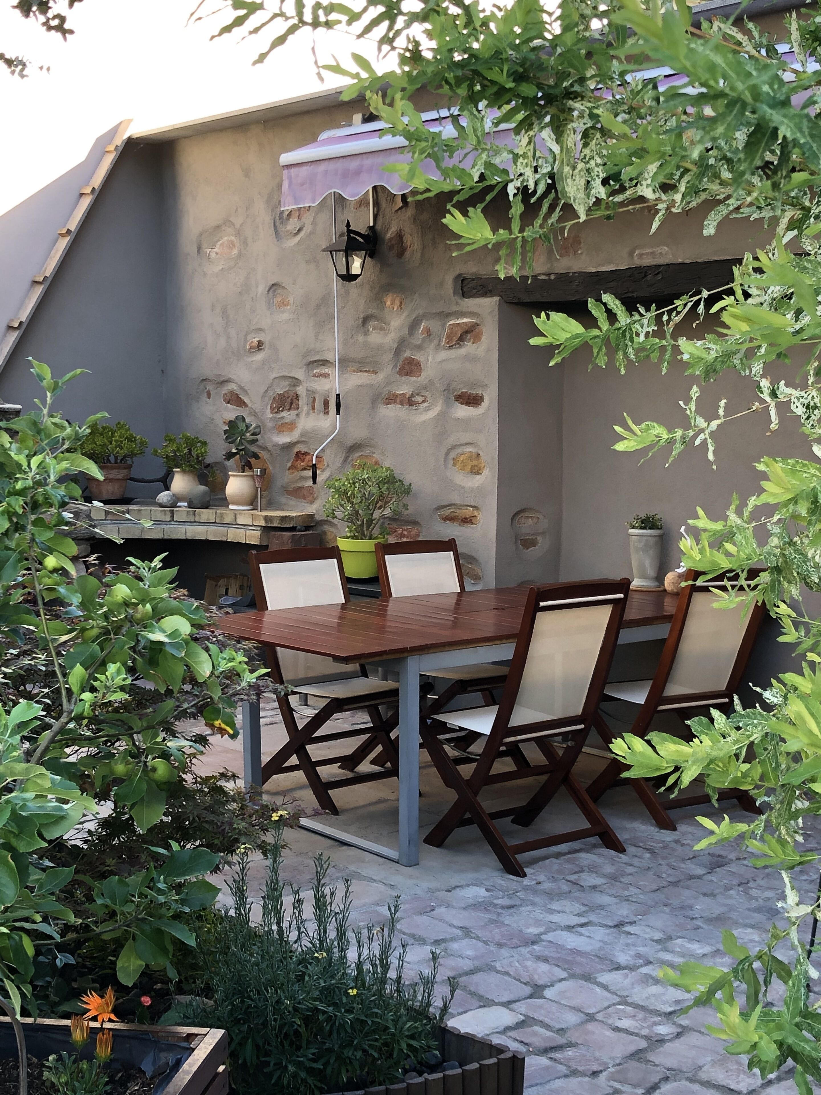 A stone wall with a built-in table and chairs, surrounded by potted plants and a small garden area.