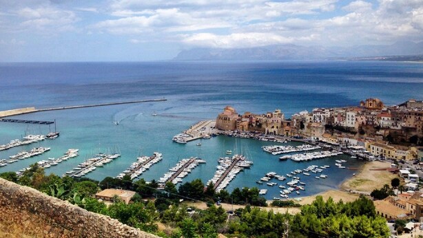 Una cittadina costiera con un porto turistico pieno di imbarcazioni, edifici storici e una vista limpida sul mare.