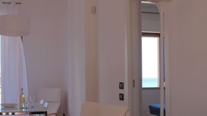 Una camera moderna con zona pranzo, una poltrona relax e vista sul mare tramite una porta aperta.