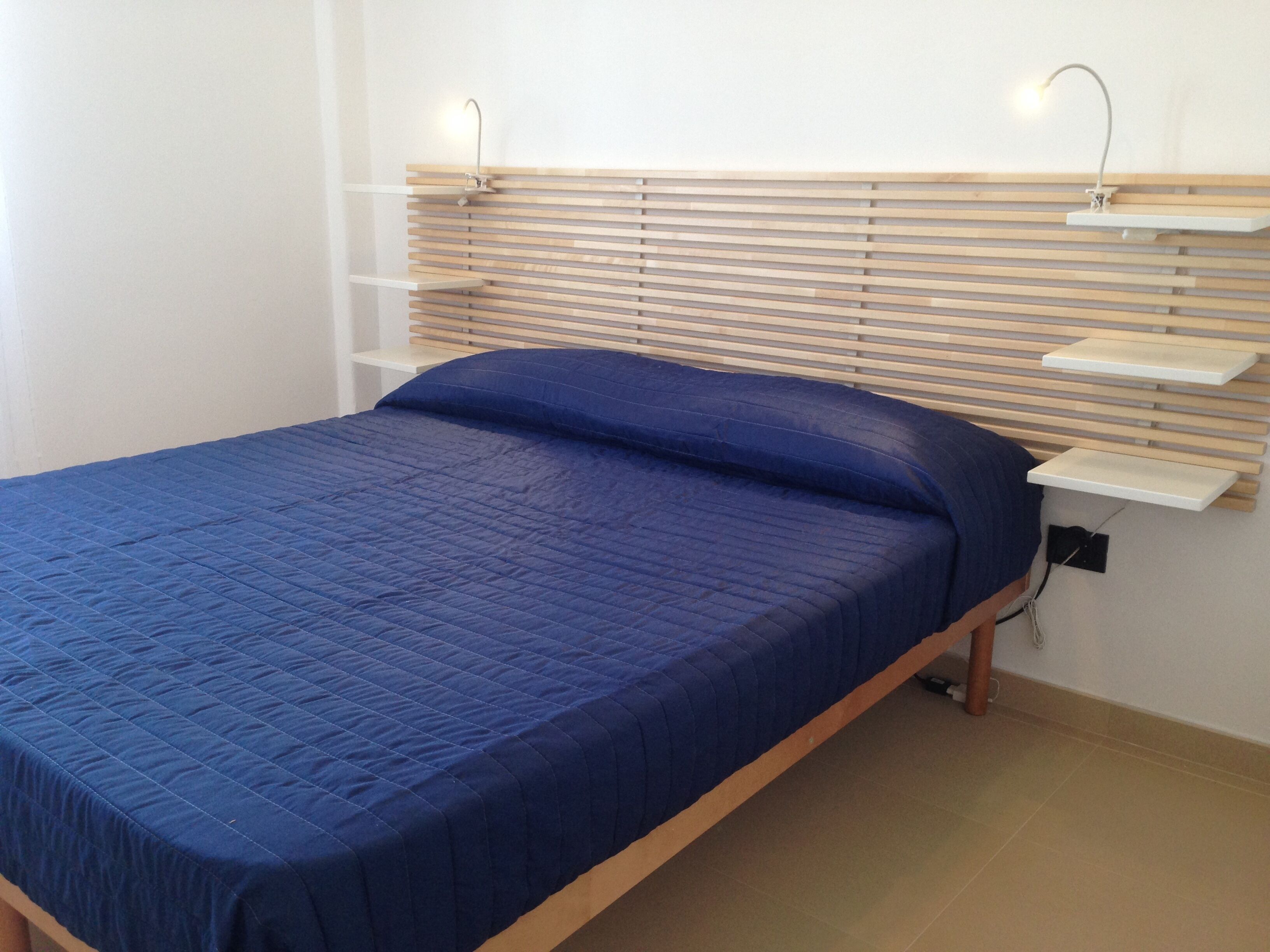 Un lit avec une tête de lit en bois, une couvre-lit bleue et deux lampes de chevet.
