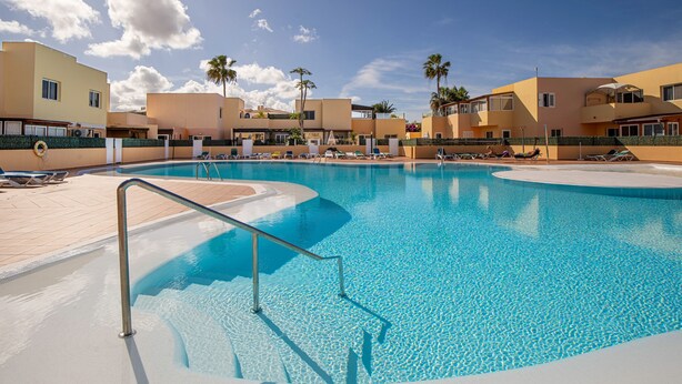 Ein Swimmingpool mit klarem, blauem Wasser, umgeben von Liegestühlen und Palmen.
