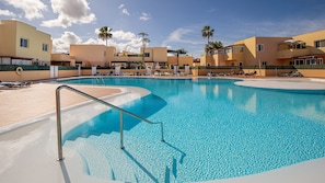 A swimming pool with clear blue water, surrounded by lounge chairs and palm trees. - APARTMENT WITH SWIMMING POOL NEAR THE SEA (Corralejo)