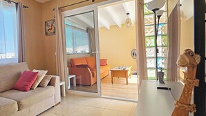 Ein Wohnzimmer mit einem beigen Sofa, einer Glastür, die auf einen Balkon führt, und einem Holzstuhl.