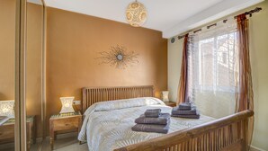 Ein Schlafzimmer mit Bett, Nachttischen, einer Wanddekoration und einem Fenster mit Vorhängen.