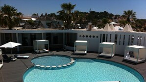 A swimming pool with lounge chairs and umbrellas, surrounded by palm trees and a building with a modern design.