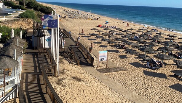 A beach with a wooden boardwalk, beach umbrellas, and lounge chairs.
