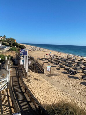 A beach with a wooden boardwalk, beach umbrellas, and lounge chairs.