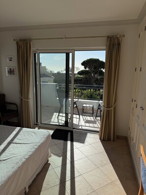 A hotel room with a bed, a chair, a small table, and a balcony with a view of the sea and trees. - Stunning villa in Vale do Lobo, private pool and high speed broadband (Vale do Lobo)