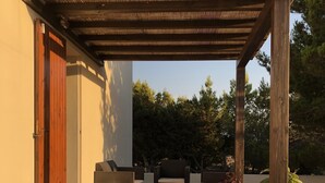 Un patio con dos sillones de descanso, una pérgola de madera y plantas en macetas.