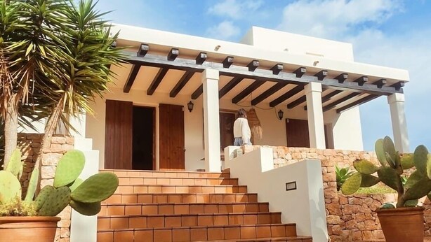 Una casa moderna con porche cubierto, escalones de piedra y cactus en macetas.