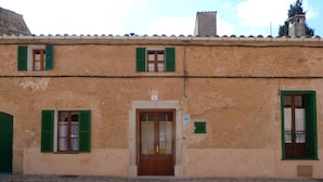 A building with a beige facade, green shutters, and a wooden door with a glass panel.