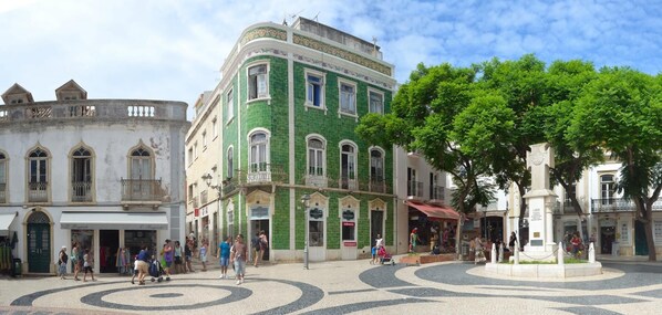 A public square with historic buildings, a fountain, and a cobblestone pavement.