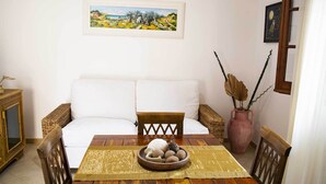 A dining area with a wooden table, white sofa, and a painting on the wall.