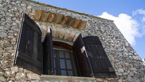 A stone building with a large window and two wooden shutters.