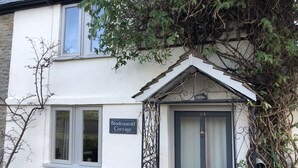 A cottage with a sign reading "Blodeuuedd Cottage," a blue door, and a small window.