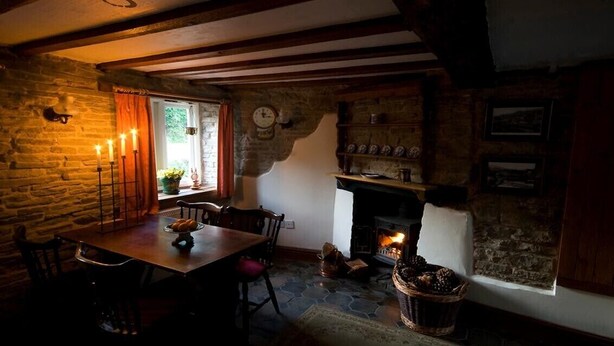 A rustic dining area with a stone wall, wooden beams, a fireplace, and a table set for two.