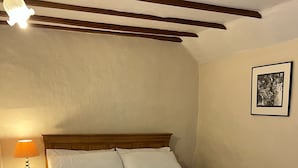 A bedroom with a wooden bed frame, white bedding, a nightstand with a lamp, and a framed picture on the wall.