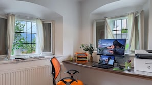 Work in comfort with a spacious desk area, equipped with a computer and printer, and enjoy a view of the outdoors through large windows.