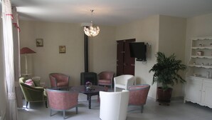 Un comedor con una mesa redonda, cuatro sillas, una lámpara de araña, un televisor, una planta en maceta y un armario blanco con estantes.