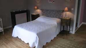 Un dormitorio con una cama, dos mesitas de noche con lámparas, un aparador y un cuadro con motivos florales.