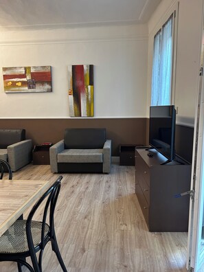 Een moderne woonkamer met een bank, een eettafel met stoelen, een flatscreen televisie en abstracte kunst aan de muur.