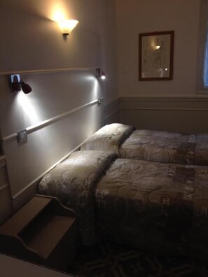 A hotel room with a bed, a nightstand, a wall-mounted lamp, and a framed picture.