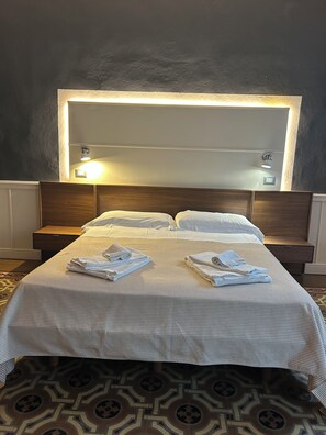 A hotel room with a large bed, a headboard with integrated lighting, a bedside table, and a patterned floor. - Max Apartment (Verona)