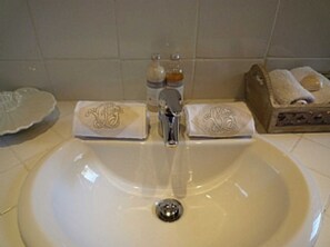 Une salle de bain avec un lavabo blanc, deux distributeurs de savon et un porte-serviettes sur lequel est posée une serviette pliée.