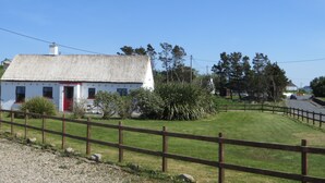 A white building with a red door, surrounded by a gravel path and a wooden fence. - Mullaghduff Thatched Cottage on the Wild Atlantic Way, near Kincasslagh, Donegal (Annagry)
