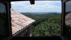 A view from a window with a tiled roof, overlooking a valley with greenery and distant hills. - Traditional hamlet house with a terrace - NEW: WIFI AVAILABLE (Vals-Les-Bains)