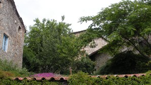 A stone building with a tiled roof, surrounded by lush greenery and flowering plants. - Traditional hamlet house with a terrace - NEW: WIFI AVAILABLE (Vals-Les-Bains)