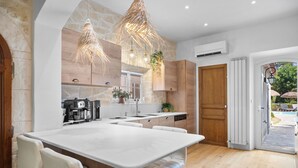 A modern kitchen with a large island, white cabinetry, and a stone accent wall. - House with garden (Saint-Cyr-Sur-Mer)