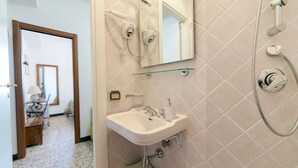 Une salle de bain équipée d’un lavabo, d’un miroir, d’un sèche-cheveux et d’une douche.