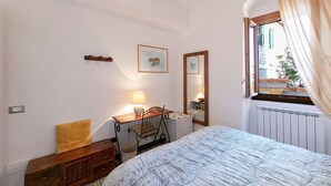 Une chambre à coucher avec un lit, un bureau avec une lampe, un miroir et une fenêtre avec des rideaux.