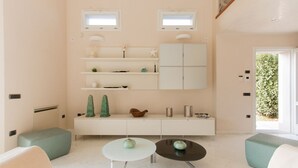 A modern living room with a minimalist design, featuring a white sofa, two round tables, and a white cabinet with shelves.