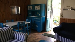 A cozy room with a dining table, blue chairs, a striped sofa, and a teal cabinet with decorative items. - houses / villas - 3 rooms - 4 persons (Groix)