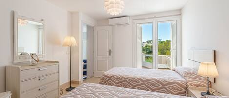 Quarto com duas camas, uma cômoda, um espelho e uma varanda com vista.