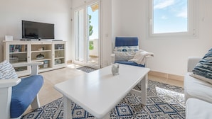 Un salon moderne doté d’un téléviseur à écran plat, de meubles blancs, d’un tapis à motifs et d’une grande fenêtre offrant une vue sur le ciel.