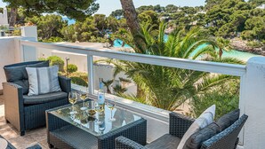 Un balcon agrémenté de meubles en osier, d’une table en verre et offrant une vue sur une plage et des arbres.