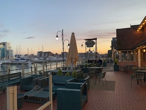 Un patio frente al agua con mesas al aire libre, vista al puerto deportivo y un edificio con el letrero 