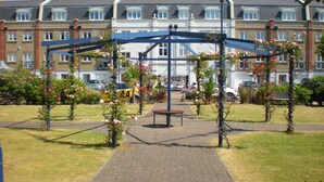 A garden with a gazebo, a pathway, and a building in the background. - Fabulously Located Marina Apartment - Superb Waterside Views from every window. (Eastbourne)