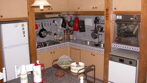 Een keuken met houten kastjes, een koelkast, een spoelbak en diverse keukengerei dat aan de muur hangt.