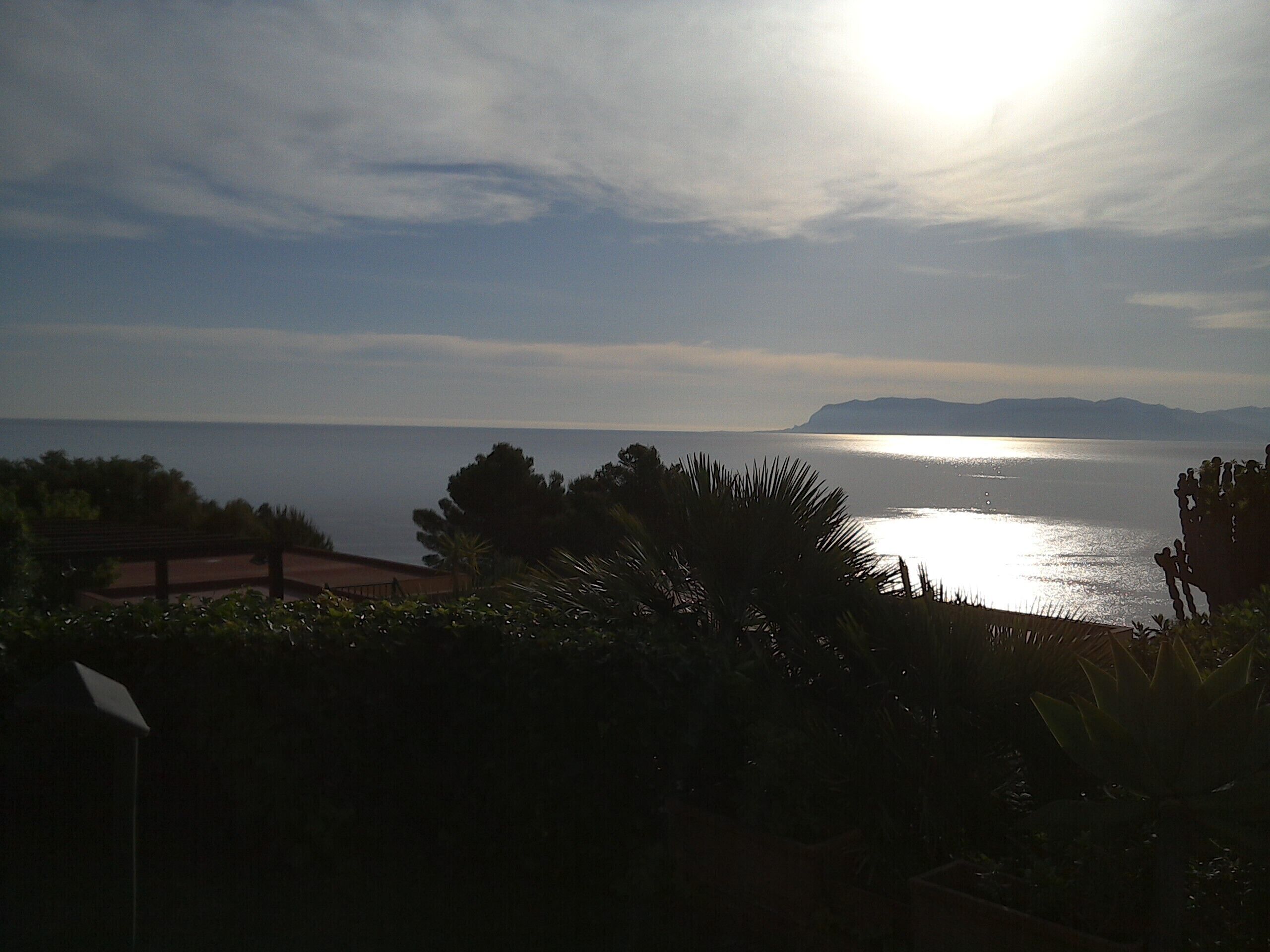 Vista costera con cielo despejado, masa de agua y montañas a lo lejos.