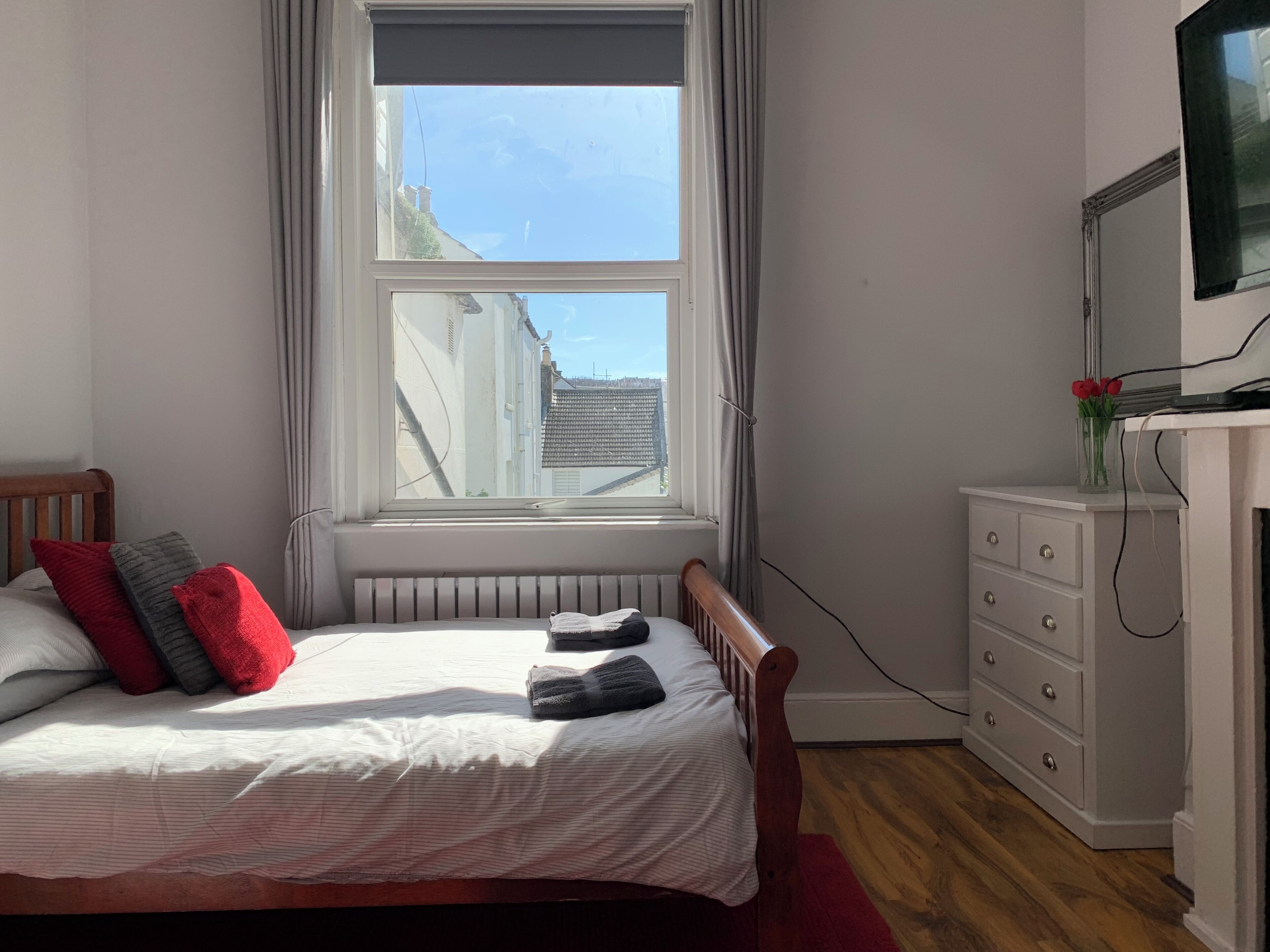 A bedroom with a bed, a dresser, a radiator, and a window with curtains.
