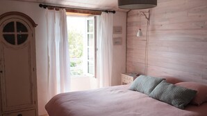Ein Schlafzimmer mit einem Bett, einem Kleiderschrank, einem Fenster mit Vorhängen, einem Nachttisch und einer Hängeleuchte.
