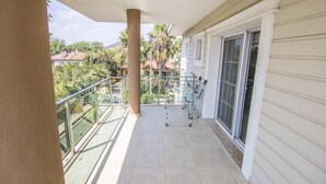 Uma varanda com guarda-corpo de vidro, um suporte de metal e vista para casas e árvores.