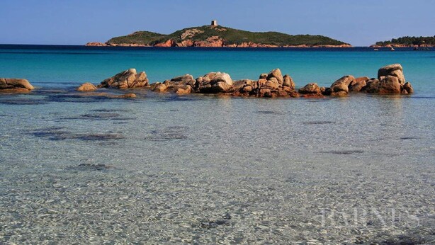 A beach with clear shallow waters, rocky formations, and a distant hill with a structure. - VILLA 4 ROOMS 3 BATHROOMS WITH  HEATED POOL  500M SEA VIEW / MOUNTAIN (Zonza)